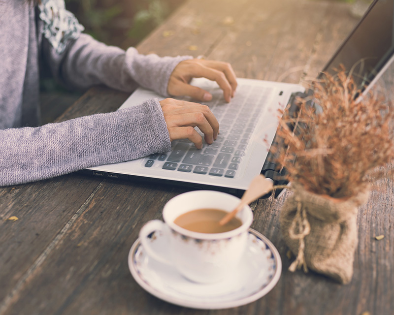 Woman sitting at a laptop with a cup of tea. Therapy for women's health in Irvine, CA